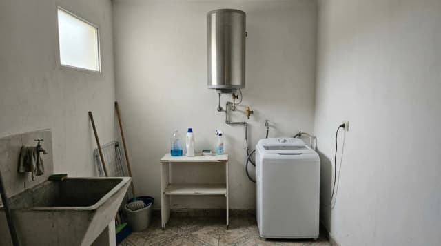 Termotanque eléctrico vertical de acero instalado en el lavadero de una casa, con sus caños de agua a la vista